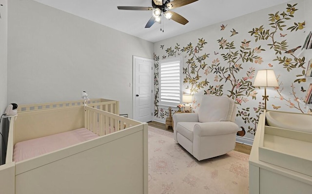 bedroom featuring a crib, wallpapered walls, baseboards, light wood-type flooring, and a ceiling fan