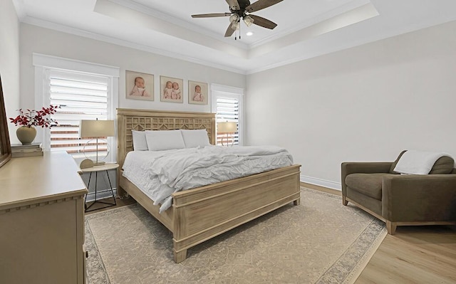 bedroom with a ceiling fan, baseboards, crown molding, a raised ceiling, and light wood-type flooring