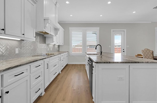 kitchen featuring an island with sink, a sink, white cabinets, crown molding, and backsplash