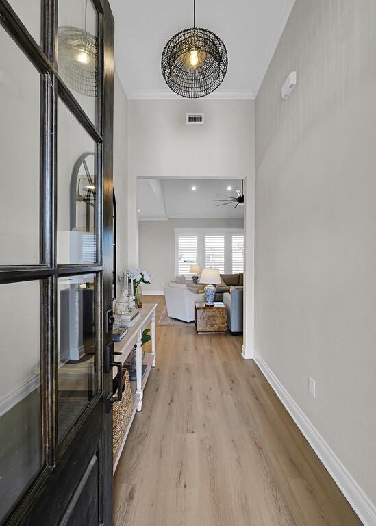 entryway with a ceiling fan, visible vents, baseboards, ornamental molding, and light wood-style floors