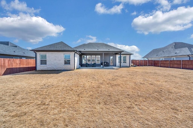 rear view of property featuring a patio, a lawn, roof with shingles, and a fenced backyard