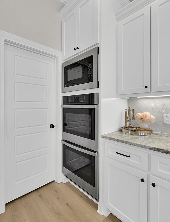 kitchen featuring light stone counters, light wood-type flooring, appliances with stainless steel finishes, white cabinetry, and tasteful backsplash