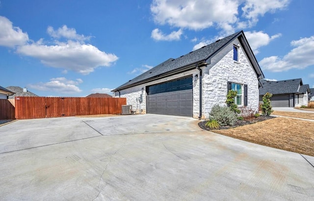 view of side of home featuring cooling unit, fence, an attached garage, concrete driveway, and stone siding