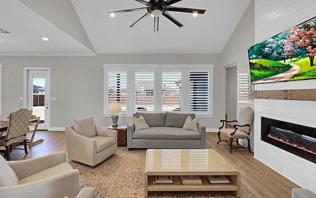 living area with a glass covered fireplace, wood finished floors, baseboards, and high vaulted ceiling