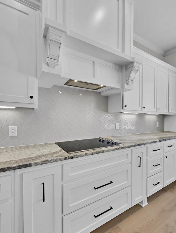 kitchen featuring light stone counters, white cabinetry, light wood finished floors, decorative backsplash, and black electric stovetop