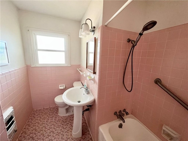 bathroom with toilet, wainscoting, washtub / shower combination, and tile walls