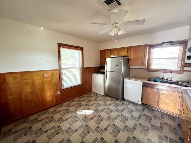 kitchen featuring wainscoting, washer / clothes dryer, freestanding refrigerator, white dishwasher, and a sink