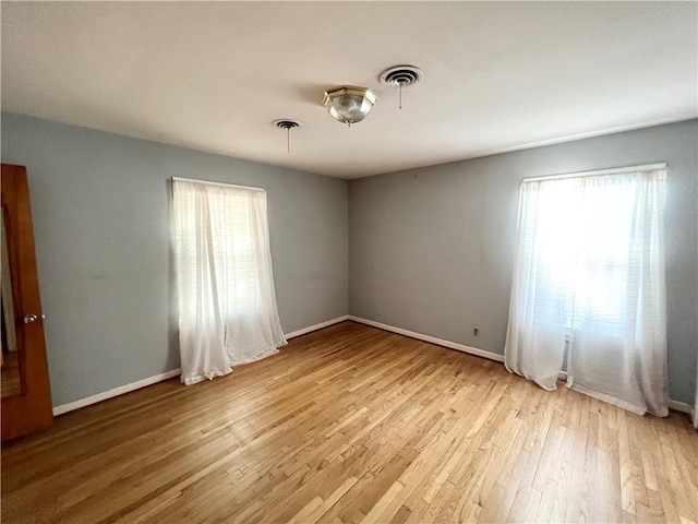 empty room with light wood-style floors, visible vents, and baseboards