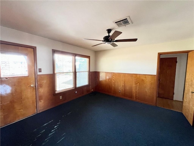 spare room featuring carpet, a wainscoted wall, visible vents, a ceiling fan, and wood walls