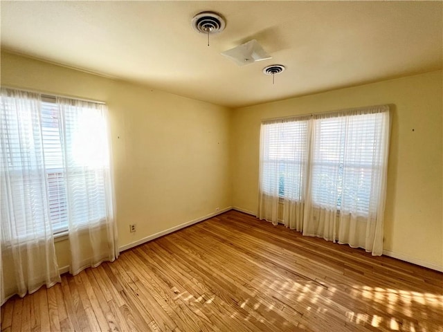 spare room with baseboards, plenty of natural light, visible vents, and light wood-style floors