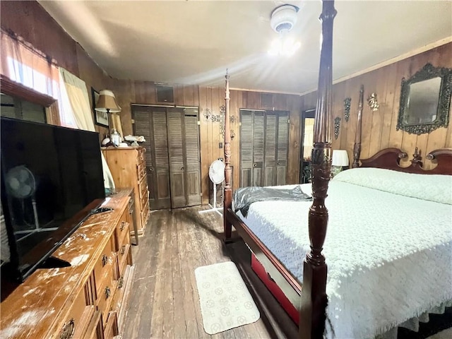 bedroom featuring two closets, light hardwood / wood-style flooring, crown molding, and wood walls