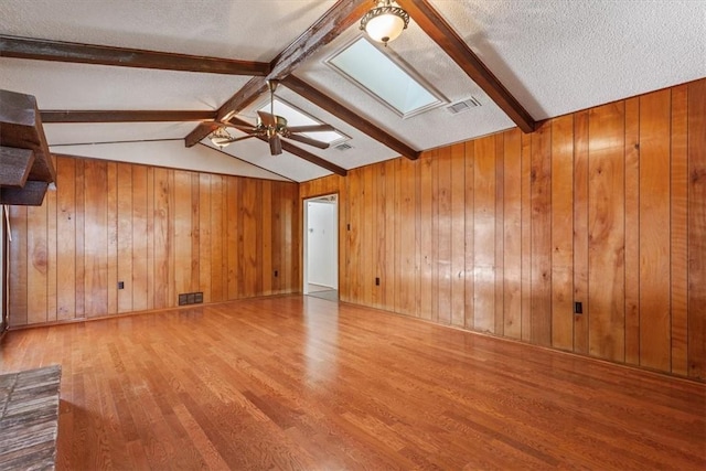 unfurnished living room featuring hardwood / wood-style floors, wood walls, vaulted ceiling with skylight, and a textured ceiling