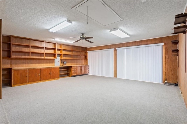 interior space with a textured ceiling, light colored carpet, ceiling fan, and wood walls