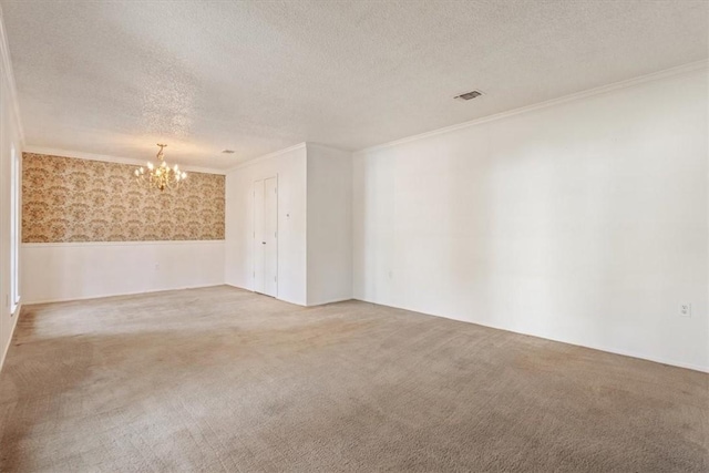 carpeted empty room with a chandelier, a textured ceiling, and ornamental molding