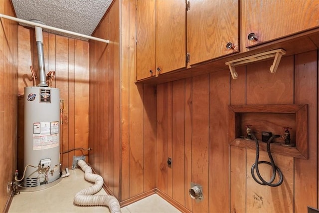 laundry area with hookup for an electric dryer, cabinets, a textured ceiling, gas water heater, and wood walls