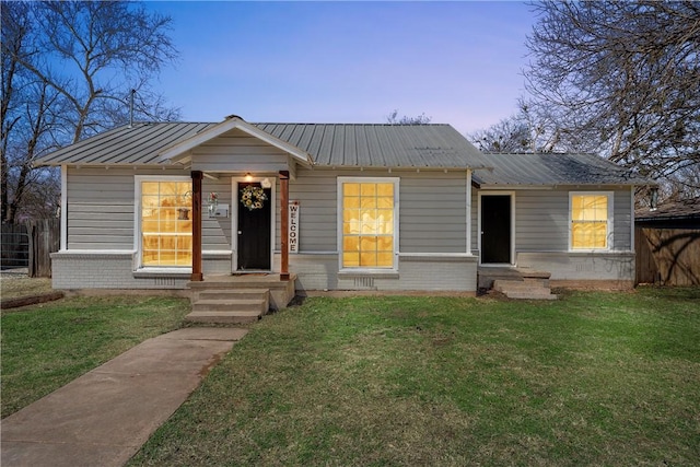 view of front of property with a front yard, metal roof, brick siding, and fence