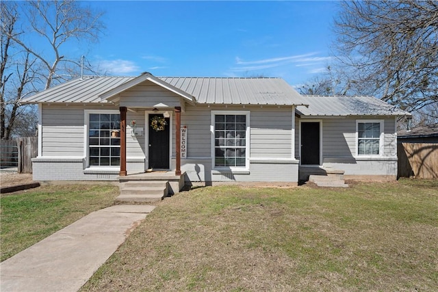 bungalow-style house featuring metal roof, brick siding, a front lawn, and fence