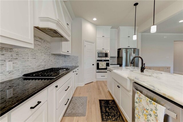 kitchen featuring stainless steel appliances, premium range hood, dark stone countertops, light hardwood / wood-style floors, and decorative light fixtures