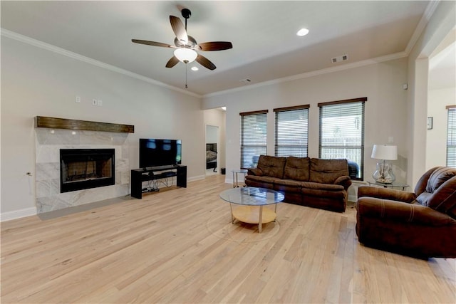 living room featuring ceiling fan, light wood-type flooring, a fireplace, and ornamental molding