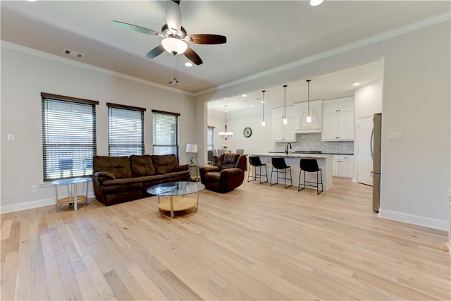 living room with ceiling fan, sink, light wood-type flooring, and ornamental molding