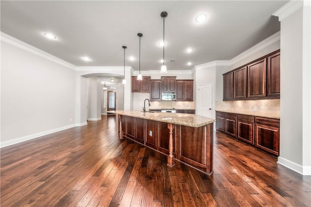 kitchen featuring dark wood-type flooring, hanging light fixtures, a center island with sink, and sink