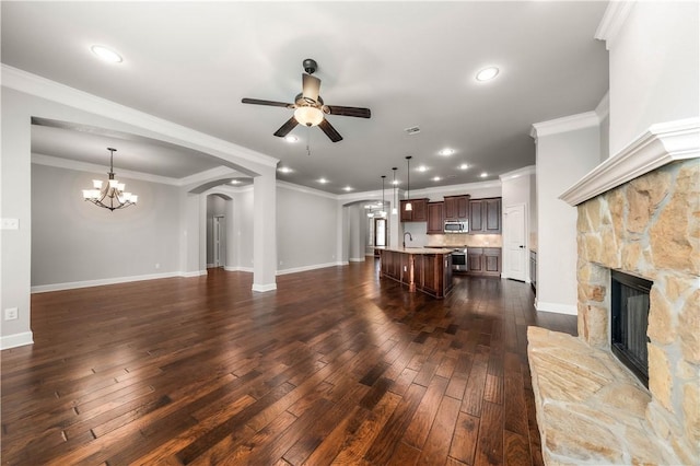 unfurnished living room with ceiling fan with notable chandelier, crown molding, dark wood-type flooring, sink, and a fireplace