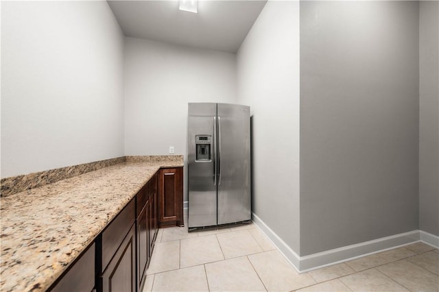 kitchen with dark brown cabinets, stainless steel fridge, light tile patterned flooring, and light stone countertops