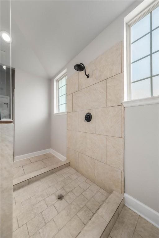 bathroom with a healthy amount of sunlight, a tile shower, and vaulted ceiling