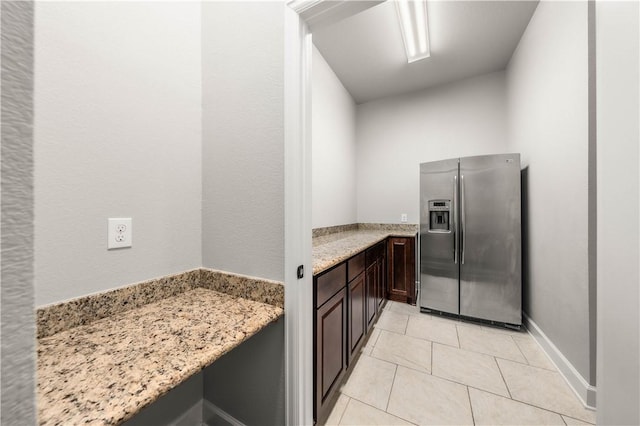 kitchen with dark brown cabinetry, stainless steel fridge with ice dispenser, light tile patterned floors, and light stone counters