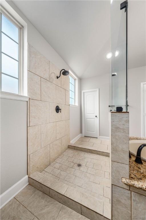 bathroom featuring a tile shower, vaulted ceiling, tile patterned floors, and a healthy amount of sunlight