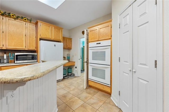 kitchen featuring light stone counters, white appliances, light brown cabinetry, and light tile patterned floors