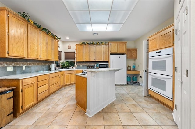 kitchen with decorative backsplash, white appliances, a kitchen island, and light tile patterned flooring