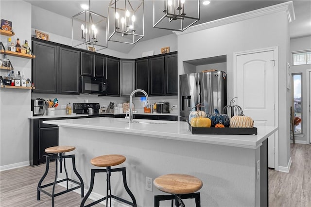 kitchen with a breakfast bar, pendant lighting, a center island with sink, and black appliances