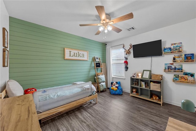 bedroom featuring ceiling fan, wood walls, and dark hardwood / wood-style floors