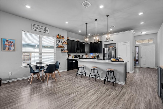 kitchen with pendant lighting, stainless steel refrigerator with ice dispenser, an island with sink, wood-type flooring, and a breakfast bar area