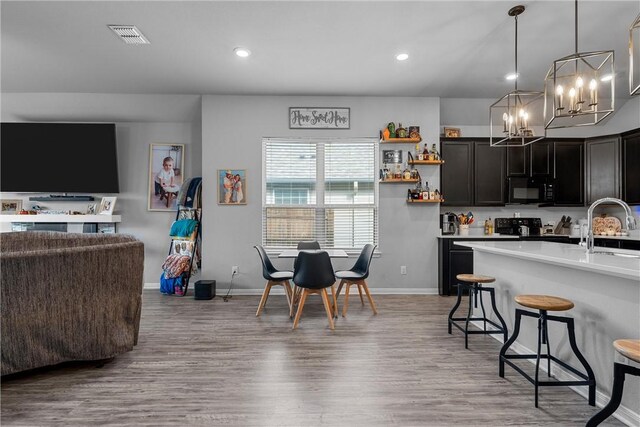 kitchen featuring hardwood / wood-style floors, a breakfast bar, black appliances, hanging light fixtures, and a chandelier