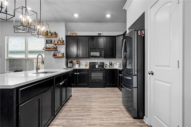 kitchen with sink, an island with sink, light hardwood / wood-style flooring, and black appliances