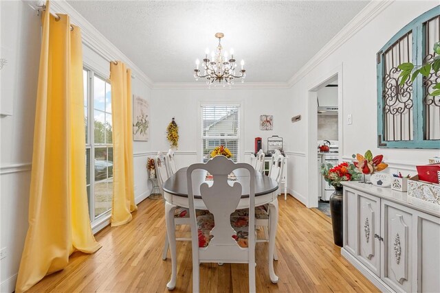 dining area with light wood-type flooring, an inviting chandelier, a healthy amount of sunlight, and crown molding