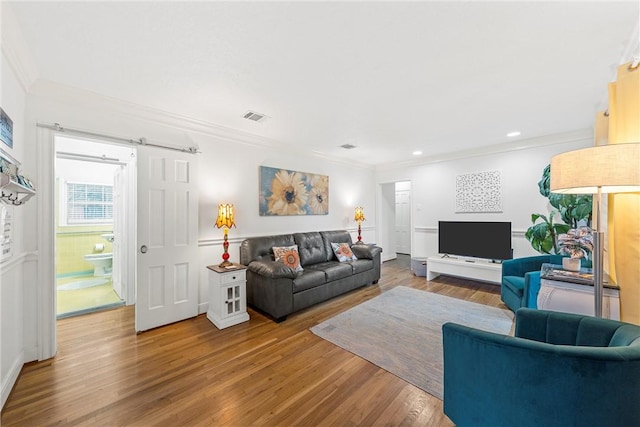 living room with a barn door, crown molding, and hardwood / wood-style floors