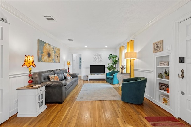 living room with built in shelves, light hardwood / wood-style flooring, and crown molding