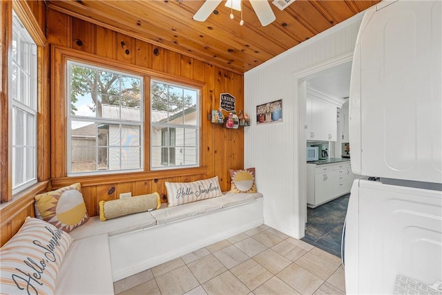 living area featuring wood walls, ceiling fan, stacked washing maching and dryer, light tile patterned flooring, and wood ceiling