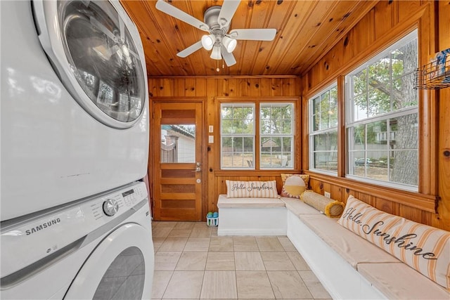 clothes washing area featuring ceiling fan, a wealth of natural light, stacked washer and clothes dryer, and wood walls