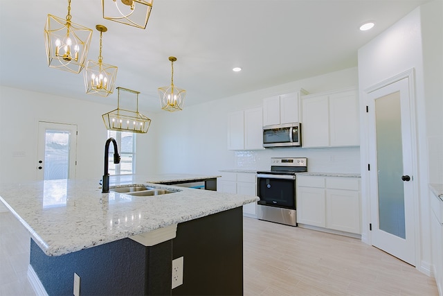 kitchen with appliances with stainless steel finishes, a kitchen island with sink, sink, pendant lighting, and white cabinetry