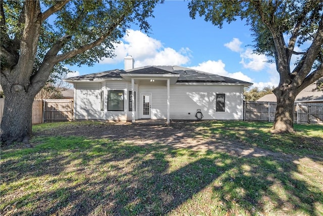 rear view of property with a lawn and solar panels