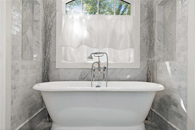 bathroom with a healthy amount of sunlight, a tub, and tile walls