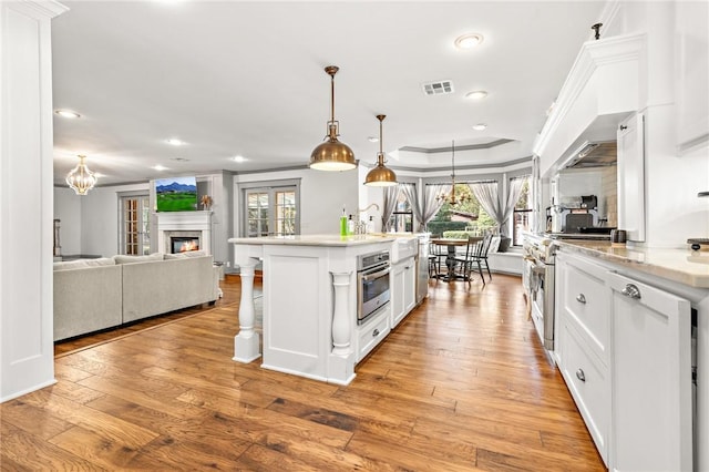 kitchen with hanging light fixtures, stainless steel appliances, a center island with sink, white cabinets, and light wood-type flooring