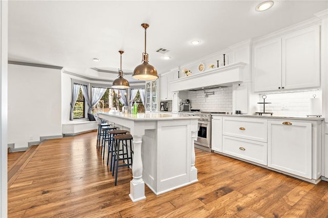 kitchen featuring white cabinets, a center island with sink, and high end stove