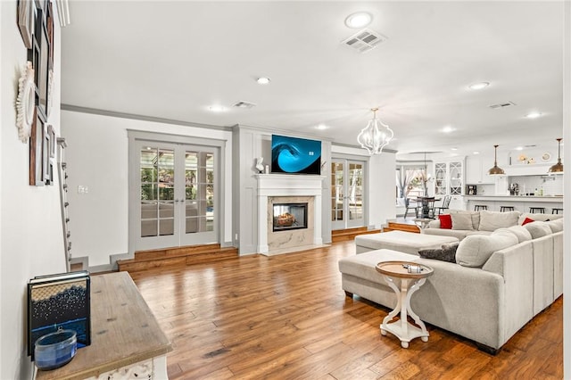 living room featuring a chandelier, french doors, light hardwood / wood-style floors, and ornamental molding