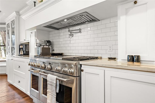 kitchen with light stone countertops, premium range hood, dark wood-type flooring, range with two ovens, and white cabinetry