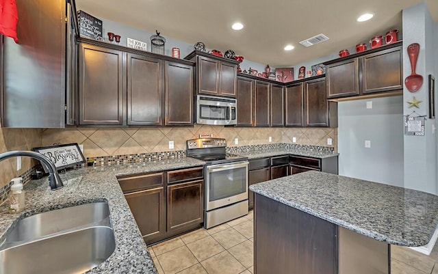 kitchen featuring dark brown cabinetry, light stone counters, sink, and appliances with stainless steel finishes